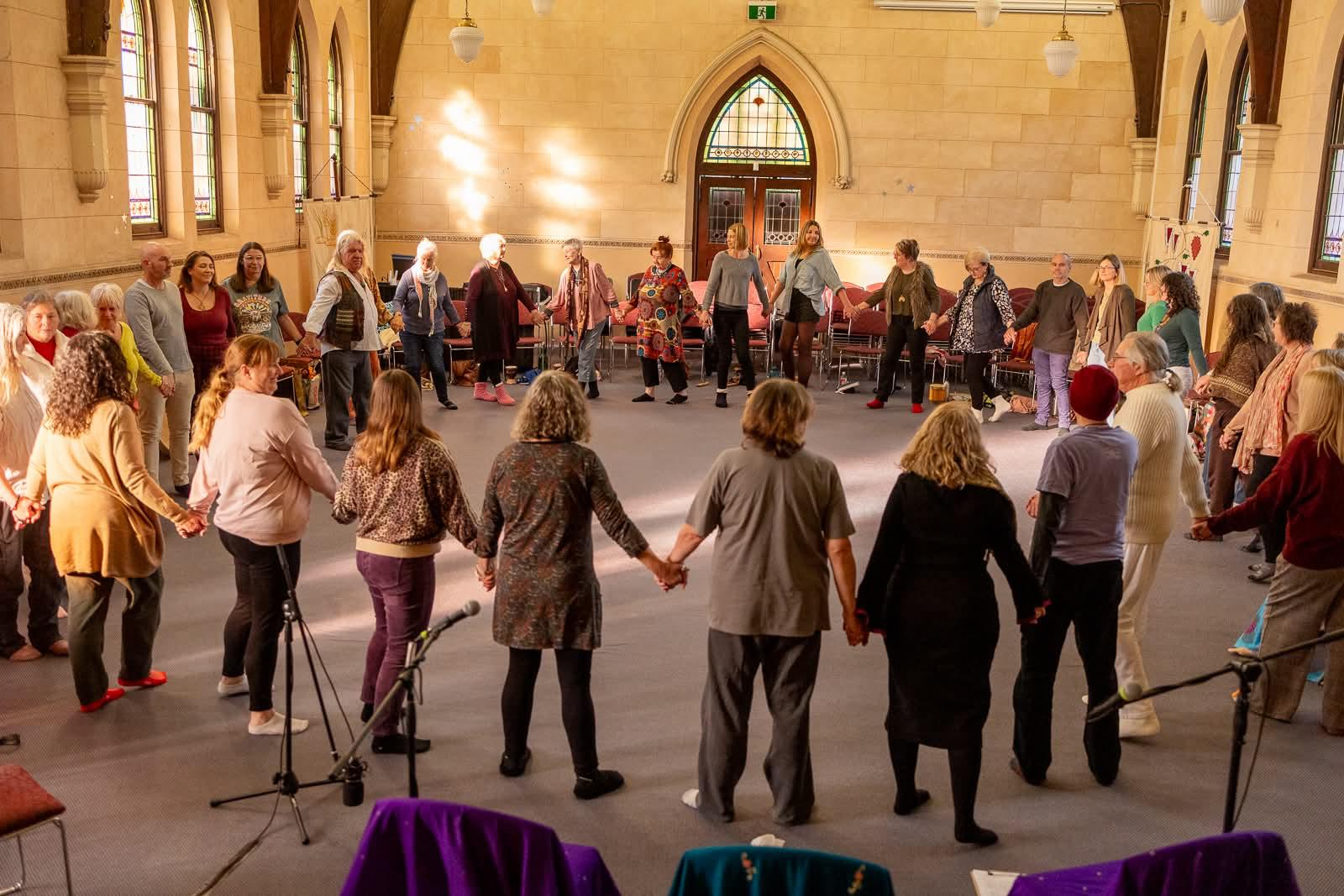 Community members gathered in a sacred circle holding hands in a beautiful historic hall